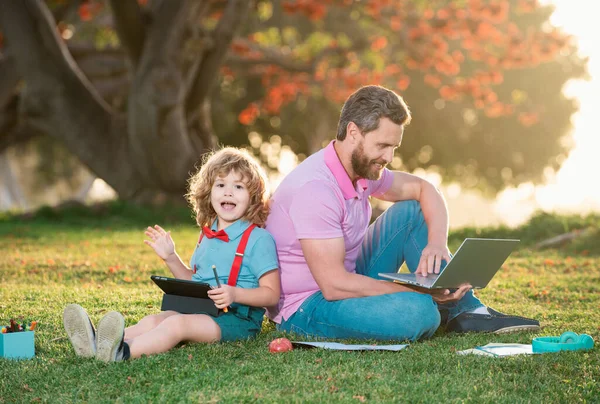 Pupil with teacher learning outdoor by studying online and working on tablet in park. Portrait of happy family father and his son using laptop outside