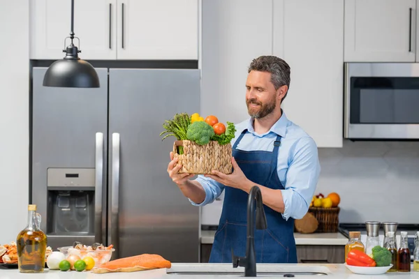 キッチンでエプロン料理のシェフ 野菜とキッチンの男 野菜とキッチンでのカジュアルな男の料理の肖像画 男調製サラダに家でキッチン — ストック写真