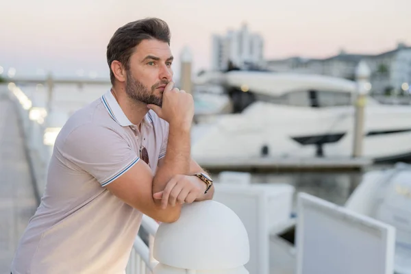 Rich business man dreaming and thinking near the yacht. Sexy man in casual clothes posing on the street. Successful male model in the urban lifestyle. Caucasian middle aged man outdoors