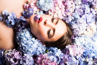 Young woman face in blooming hydrangea in background. Romantic and love concept. Nature beauty. Woman lying on flowers. Makeup cosmetics and skincare. Girl with hydrangea flowers