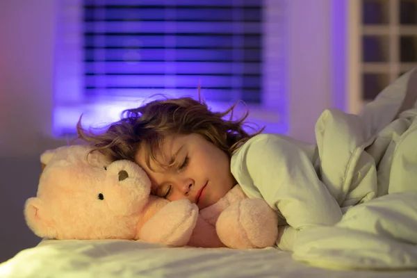 Good night sleep. Adorable kid sleeps in bed with a toy teddy bear. Sleeping child