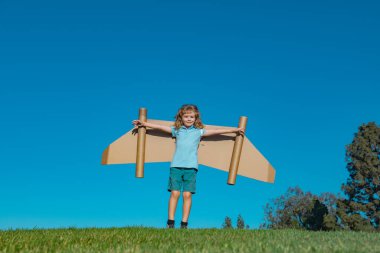 Kartondan oyuncak uçak kanatlarıyla oynayan çocuk gökyüzünde metin için fotokopi alanı ile uçuyor. Aile yaratıcılığı ve uçma hayali.
