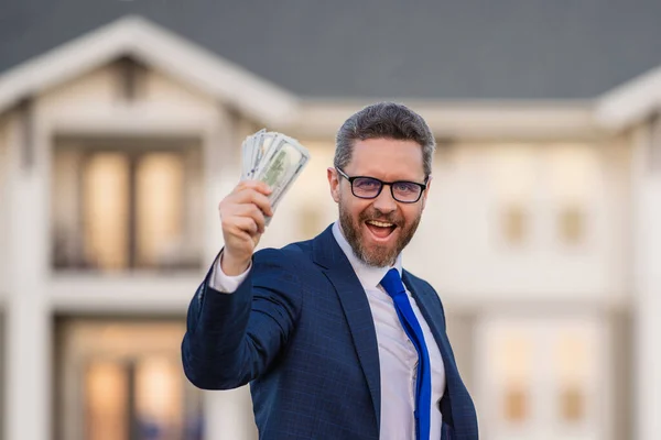 Real estate agent, broker or owner front of property. Outdoor portrait of man with money banknotes. Dollar bills, credit, online banking. Rich man with dollar banknotes, bank loan, financial savings