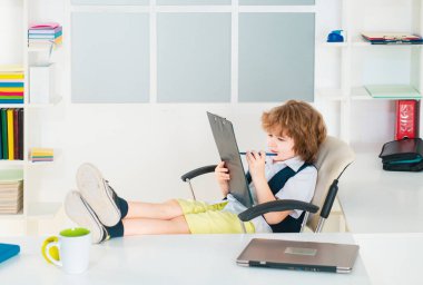 Başarılı küçük çocuk işadamı ofiste oturuyor. Serbest çalışan bir çocuk gibi giyinmiş.