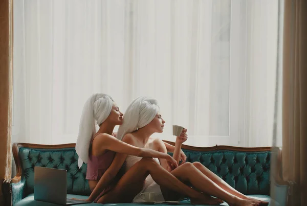 現代的なホテルでラップトップ付きのベッドで朝食を持っている魅力的な女の子 楽しい女友達がリビングでベッドに寝そべって — ストック写真