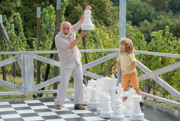 stock image Grandfather and grandson playing chess on big chess board. Elderly old relative wit child