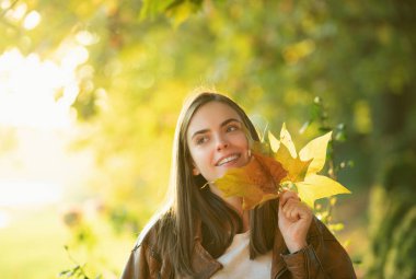 Güzel kadın yüzünün yanında sarı yapraklar tutuyor.