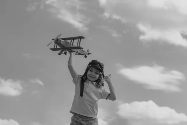 Child boy with pilot goggles and helmet playing with wooden toy airplane, dream of becoming a pilot. Childrens dreams. Child pilot aviator with wooden plane. Summer at countryside