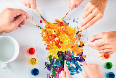 Sanat malzemeleri olan yaşlı ve genç eller. Anne, baba ve çocukların elleri renkli kalemlerle çizim yapıyor.