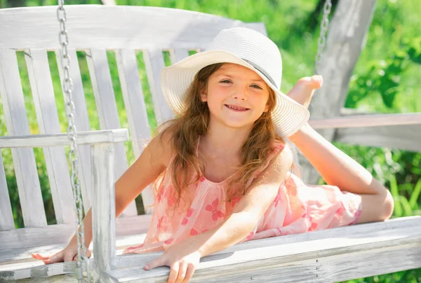 stock image Child dreaming. Happy child girl laughing and swinging on a swing at the park in summer. Kids happiness and smile. Close up portrait of a beautiful child girl in hat dreaming. Dreamy kids face