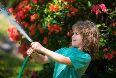 Bahçedeki çiçekleri sulayan çocuk. Çocuk şefkati ve çocukluk kavramı. Küçük yardımcı. Güzel sarışın çocuk yazın evin içinde su hortumunu tutuyor.