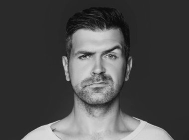 Tüylü ve kaşlı yakışıklı bir adamın portresi. Gri arka planda, dikey resimde, stüdyoda ileri bakan bir model.