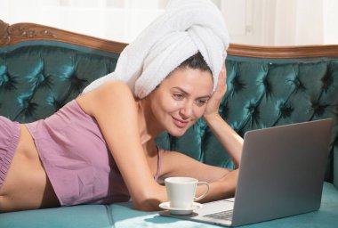 Rahat bir iş yeri serbest çalışan bir kadın için çalışıyor. Evde dizüstü bilgisayarla çalışan mutlu sıradan bir kadın. İnternette kahve ve dizüstü bilgisayarla sohbet eden kadın modeller yatak odasındaki kanepede dinleniyorlar.