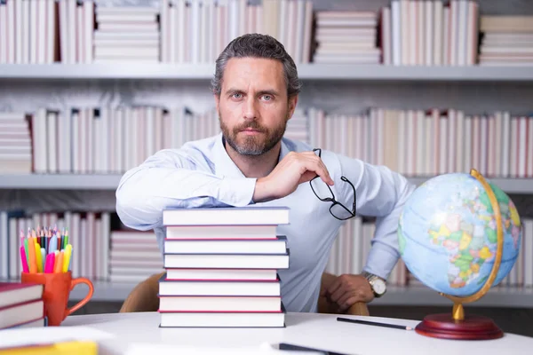 Portrait of school teacher with book in classroom. Handsome teacher in classroom. Teachers Day. Good school teacher. Tutor at classroom. Man with books in classroom. Knowledge and education concept