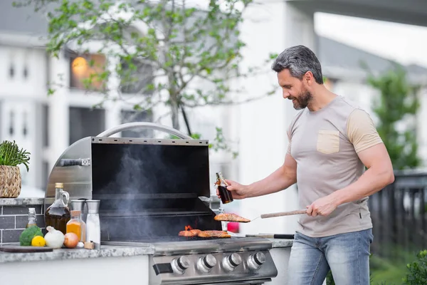 バーベキューの準備をしてる40代の男 男性はバーベキューグリルで肉を調理します 男はバーベキューで肉を調理夏の家族の夕食のために家の裏庭で — ストック写真