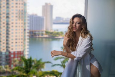 Sexy woman on terrace. Young lady in stylish shirt poses on balcony and enjoys spring. Girl on terraced house by the sea, enjoy morning fresh air with ocean. Sensual woman enjoy town view at terrace