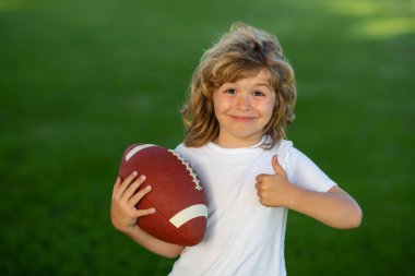 Açık hava çocukları spor aktiviteleri. Amerikan futbolu ya da parkta rugby oynayan Amerikalı bir çocuk. Sportif çocuklar. Futbolcu topu tutuyor