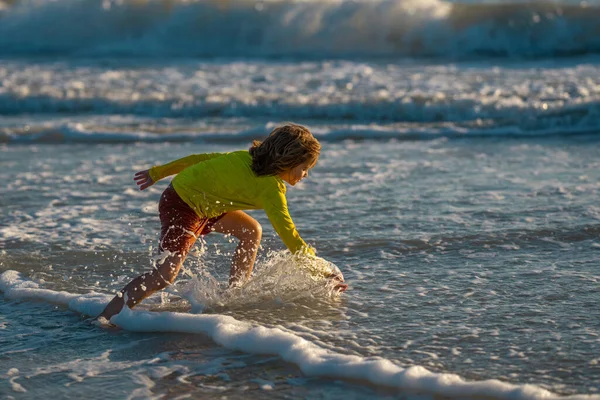 子供の男の子が日の出にビーチを走っている 海のビーチで走っている幸せな驚きの子供 夏の日に海の近くを走るかわいい子供 子供たちは熱帯のビーチで楽しみを持っています スプラッシュ海の水で子供の遊び — ストック写真