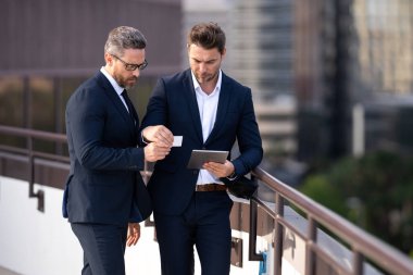 İş ekibi, takım çalışması ve işbirliği. İş adamları dışarıda tablet bilgisayar kullanıyor. İş adamları şehir planındaki iş başarılarıyla tablet arıyorlar.