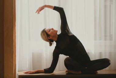 Ev antrenmanı. Evinde yerde esneme egzersizleri yapan bir kadın. Spor kıyafetleri içinde genç bir kadın pencere kenarında egzersiz yapmadan önce esneme hareketleri yapıyor. Vücuda ve zihinsel sağlığa uygun.