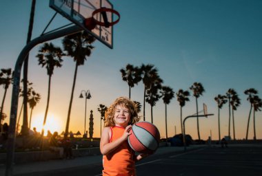 Çocuk basketbolcunun portresi. Çocuk basketbol topunu Venice plaj sahasında tutuyor.