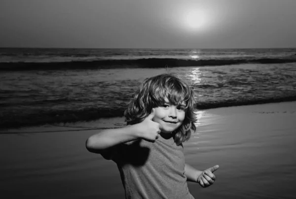 夕日のビーチで面白い子供の男の子 親指を上げる 驚くべき子供の感情 — ストック写真