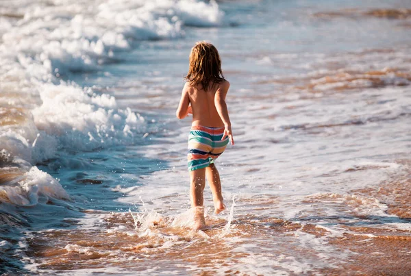 海辺の近くでビーチを実行している少年のバックビュー 海や海で水を駆け抜ける楽しさを持つ興奮した驚きの子供 — ストック写真