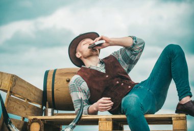 Erkeklerin güzellik standardı. Gerçek erkekliğin bir örneği. Şapkalı bir kovboy. Batı hayatı. Kovboy şapkalı, ekose gömlekli, alkol içen traşsız bir adam. Yakışıklı sakallı maço adam.