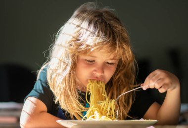 Makarnalı makarna yiyen komik çocuğun portresi. Küçük çocuk mutfakta kahvaltı yapıyor.