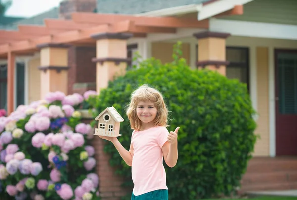 Kid dreaming of new home. Happy boy holding dream house, show thumbs up. Home insurance concept. Mortgage, house insurance, future plans, protecting children