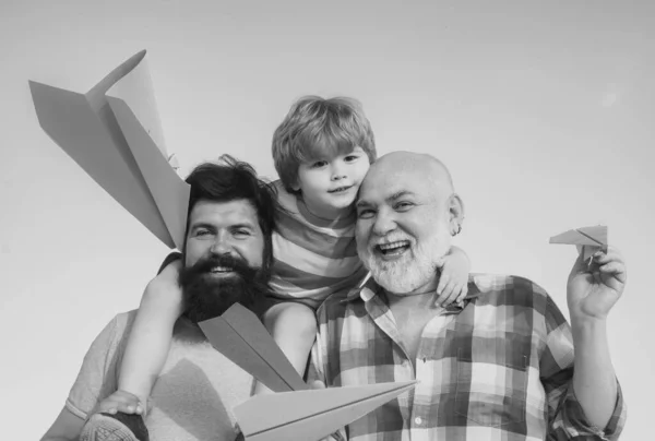 多世代 幸せな父親の肖像画は 息子のピギーバック彼の肩に乗って検索を与える 夏の空を背景にしたおもちゃの紙飛行機で遊ぶ幸せな子供 — ストック写真