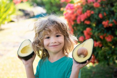 Bahçedeki mutlu çocuk avokadoyla eğleniyor. Çocuklar yaz vitamini