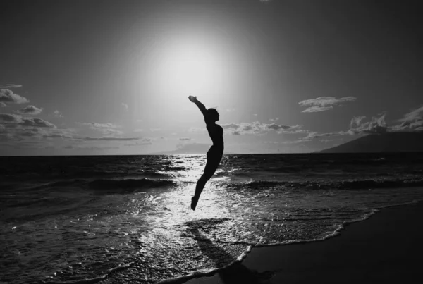 一个无忧无虑的女人 高举双手 在大海和蓝天的映衬下跳跃着 旅行和自由的概念 — 图库照片