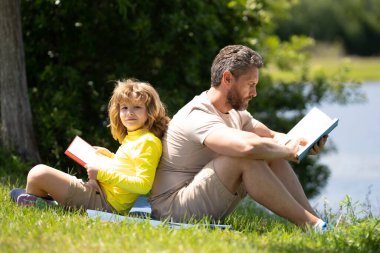 Ot üzerine kitap okuyan sevimli bir aile. Oğlan ve baba parkta piknik yapıyorlar. Mutlu oğul ve baba kitap okuyor. Mutluluk ailesi. Babam parkta çimlerin üzerinde oturan bir çocuğa kitap okuyor.