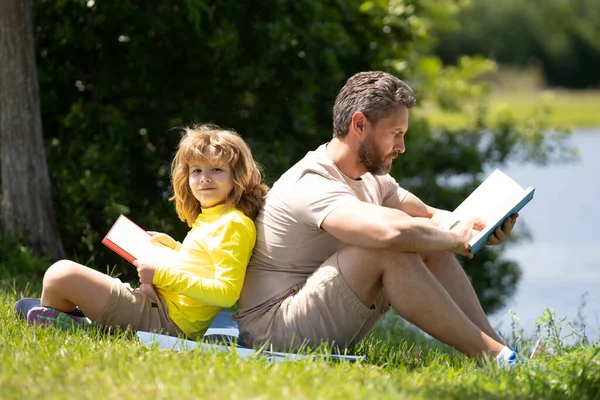 Stock image Lovely family reading a book on grass. Boy and dad having a picnic in park. Happy son and father reading a book. Happiness family. Father reading a book to child sitting outdoor on the grass in park