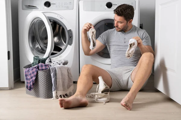 stock image Man with clothes near washing machine. Handsome man sits in front of washing machine. Loads washer on laundry. Man cleaning clothes. Housework for single alone guy. Home laundry