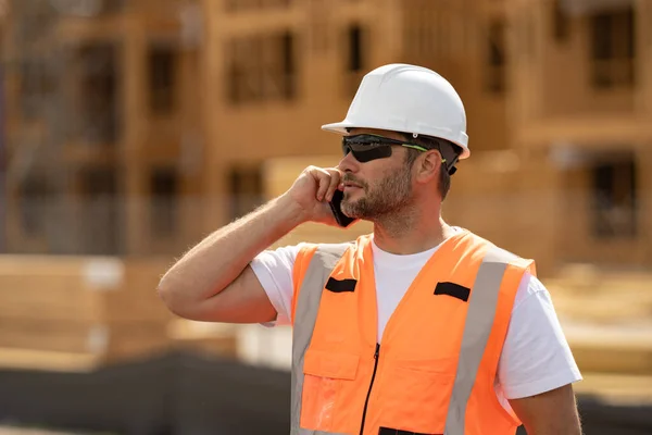 大楼建筑背景下穿着制服打电话给工人 建筑工地的建筑商 建筑工地上戴头盔的男工 戴硬礼帽的硬汉 — 图库照片