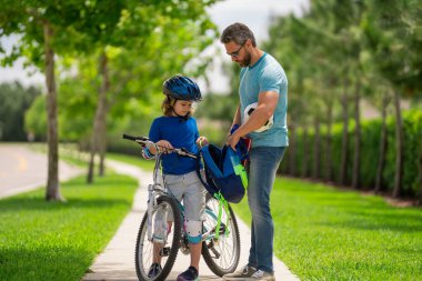 Baba oğul kavramı. Baba oğluna bisiklet sürmeyi öğretiyor. Baba oğlunun Amerikan mahallesinde bisiklet sürmesine yardım ediyor. Kasklı çocuk babasıyla bisiklet sürmeyi öğreniyor. Babalar Günü