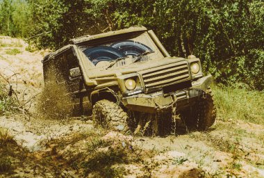 Dağların arasında bir kamyonet. 4x4 yolculuk gezisi. Jeep su birikintisine çarptı ve toprak püskürttü. Aşağıdan büyük off-road araba tekerleği kırsal yolda ve dağların gerisinde