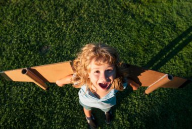 Gülen çocuk yaz parkında oyuncak uçak kanatlarıyla oynuyor. Yenilik teknolojisi ve başarı konsepti. Çocuk pilot parkta çimlerde eğleniyor.