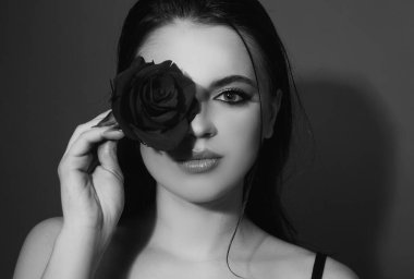 Brunette woman with blue eyes and red rose. Beautiful girl with reses flowers. Closeup face of young beautiful woman with a healthy clean skin and bright makeup