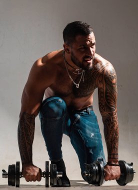 Dambılla egzersiz yapan kaslı adam. Sportif adam çalışıyor. Gri arka planda kaslı gövde. Güç ve motivasyon. Güçlü vücut geliştirici, karın kasları, omuzları, göğüs kasları var.