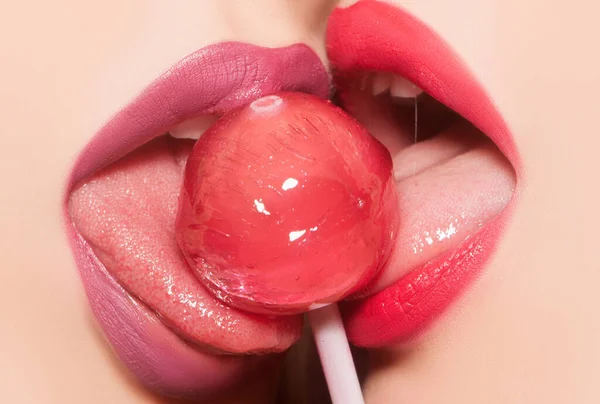 性感女性的嘴舔 同性恋口头上的快乐 两只性感艳丽的女性唇 嘴里含着粉色和紫色唇彩 舔着香甜圆圆圆的红棒糖的合影 — 图库照片