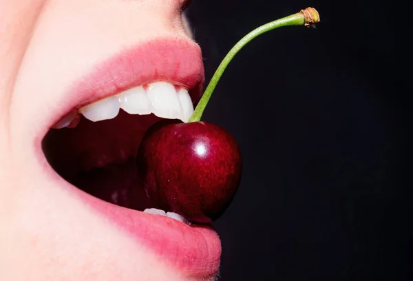 Summer sexy fruits. Cherry in teeth, macro, close up. Cherry in woman mouth. Cherries on woman lips. Girl biting cherry. White teeth, dental background