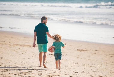 Baba ve çocuk dışarıda eğleniyor. Baba ve oğul yaz plajında yürüyor. Çocukluk ve ebeveynlik kavramı