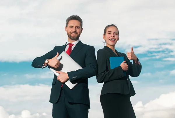 Portrait of smiling business people with thumbs up. Successful business couple. Successful business people standing over blue sky