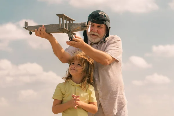 Grandfather and grandson having fun with toy plane on sky. Child dreams of flying, happy childhood with granddad. Family dream. Child dreams with plane. Grandfather and child son dream. Daydreamers