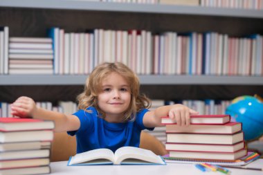 Küçük öğrenci kitap okuyor. Okul kütüphanesindeki masada ödev yapan okul çocuğu. Öğrenci çocuk kitap yığınının yanında ödev edebiyatı okuyor. Çocuk kitaplarla dolu bir kitap okuyor.