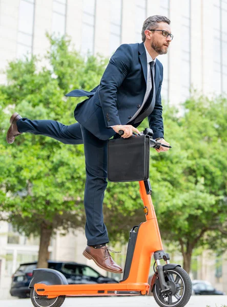 Scooter allows business man in suit to be efficient and punctual. Electric scooter provides a quick and easy for business man. Electric scooter helps funny business man make up for lost time. Fast