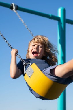 Playground. Kid swinging on swing on playground. Craziness and freedom. Young summer child playing on swing outdoor. Crazy playful child swinging